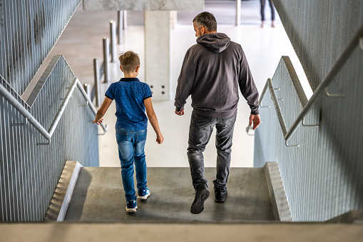 Rear view of father and son walking on staircase.