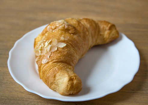 Croissant with almond flakes on a white plate. Homemade puff pastry. Croissant with a ruddy crust in close-up. fresh bakery. traditional French breakfast