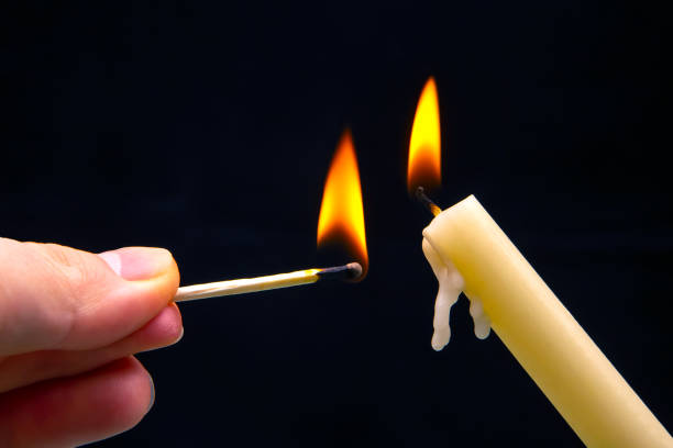 istock Lighting a candle with a wooden match on a dark background. Burning candle fire 1483519413