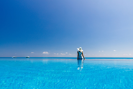 Rear view of a carefree woman sitting at the edge of an infinity pool and looking at view. Copy space.