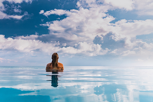 Back view of a woman spending her summer day in infinity pool and looking at view. Copy space.