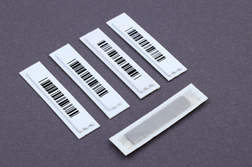 Magnetic AM label with barcode: the necessary protection even for small products. Plastic White Barcode Soft Tags on gray background. Retail security.