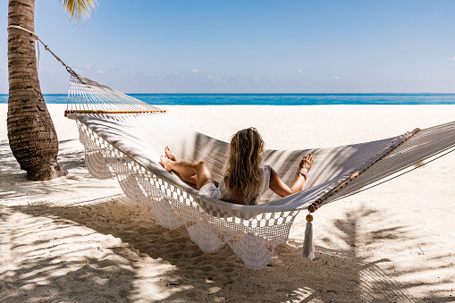 Relaxed woman spending her summer day in hammock on the beach and looking at view. Copy space.