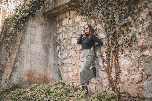 Portrait of a beautiful and smiling modern woman standing leaning against a wall in nature