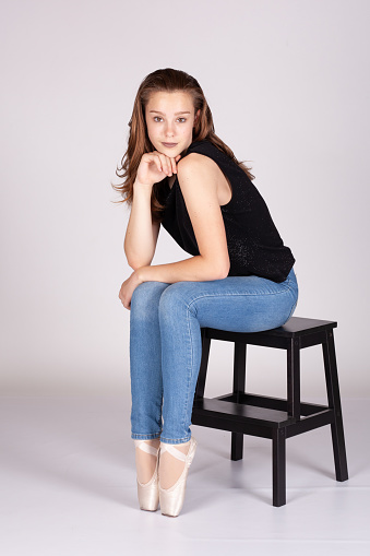 En Pointe resting on stool legs together coy expression looking at the camera hand to chin in a shrug en pointe Beautiful teen girl looking quizically with machiavellian tendencies Metaphor image for meme