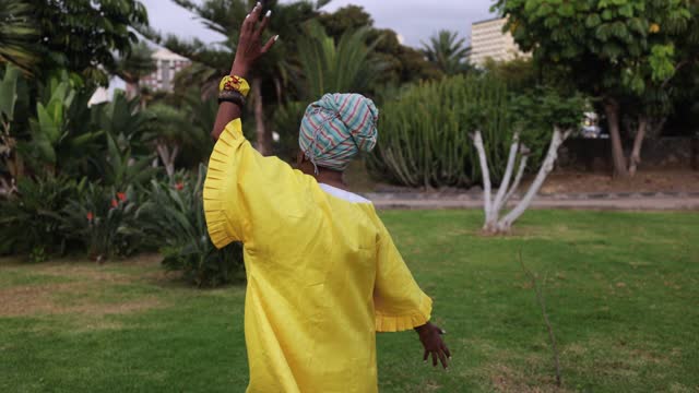 African senior woman dancing at park while wearing traditional afro dress and turban