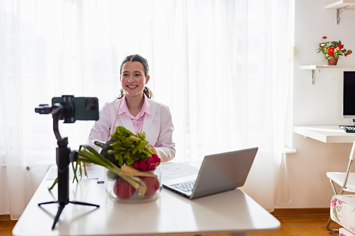 Young female nutritionist in lab coat sits confidently in front of the camera, sharing her knowledge and tips for a healthy lifestyle