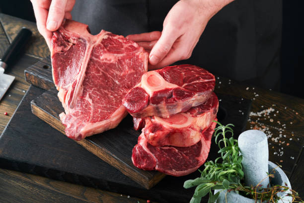 istock Steak beef meat. Chef cutting steak beef. Mans hands hold raw steak Tomahawk on rustic wooden cutting board on black background. Cooking, recipes and eating concept. Selective focus. 1483530947