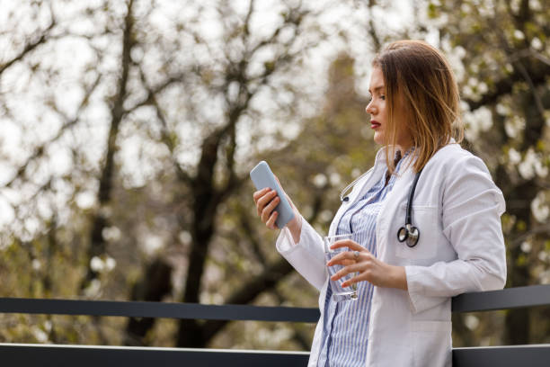 istock Young female doctor standing on the balcony, taking a break from work and using smart phone 1483532865