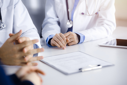 istock Group of unknown doctors are sitting at the desk and discussing problems or disease treatment in sunny hospital office. Covid 2019 1483535060
