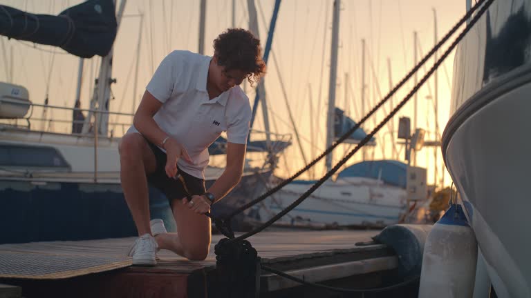 Sailing, yacht and deckhand with rope working on luxury charter cruise for summer holiday at sea. Water, adventure and travel, man on jetty getting sail boat race ready for ocean journey at sunset.