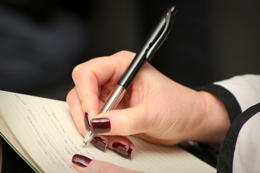 A close-up of a person's hands writing notes in a notebook, with a pen in her hand