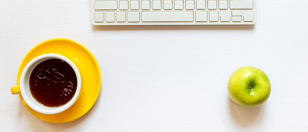 Healthy snack with working in the office.  Green apple yellow cup black coffee for diet Health life with keyboard on white wood background.  Healthy Lifestyle Concept, top view, copy space for banner
