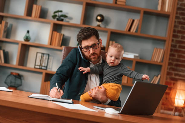 istock Conception of multitasks. Businessman in formal clothes is working indoors. With toddler 1483544077