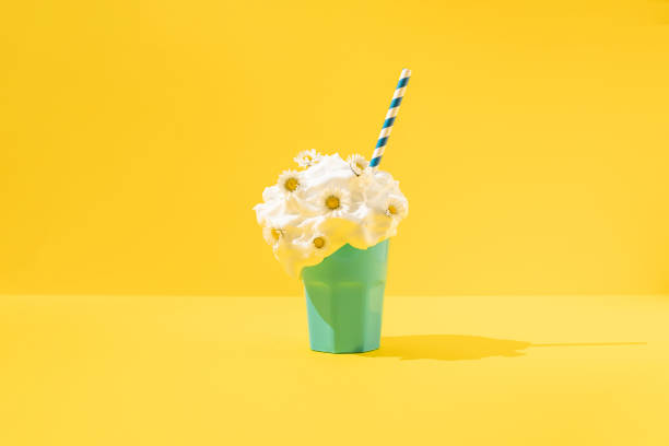 Creamy milkshake with daisy flowers and paper straw on yellow background. Copy space.