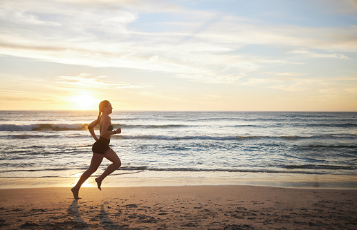 Woman, fitness and running on the beach in sunset for healthy cardio exercise, training or workout in the outdoors. Female runner exercising in sunrise for run, health and wellness by the ocean coast