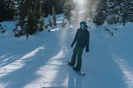 A man smiles at the camera while snowboarding in Oregon on a sunny winter day.