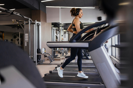 Woman running on a treadmill in an empty gym with headphones on