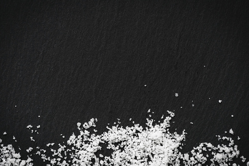 Sprinkled organic sea white salt on a black slate stone background. Concept of cooking natural healthy food. Copy space.
