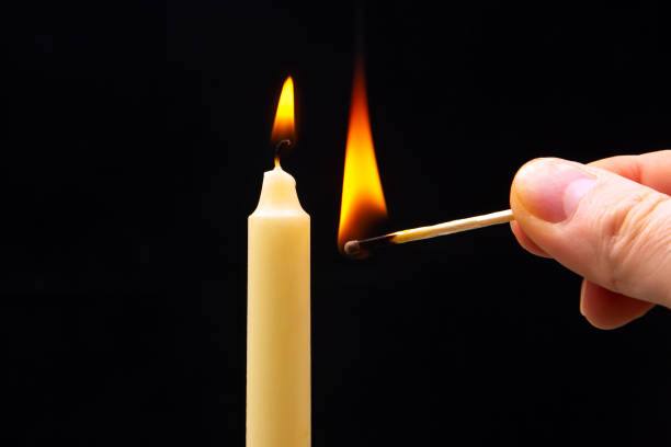 istock Lighting a candle with a wooden match on a dark background. Burning candle fire 1483559408