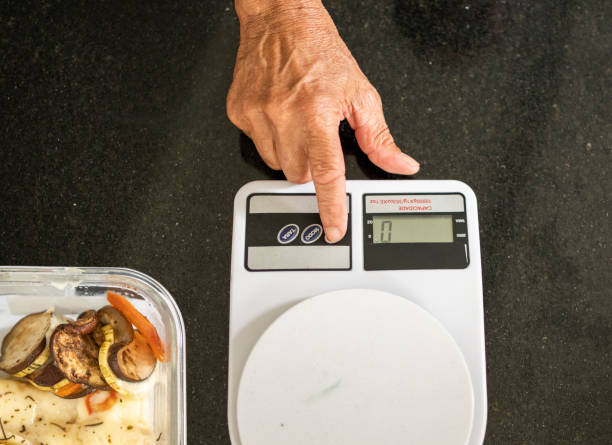 High angle close-up of a senior man weight a container of leftovers on a scale sitting on a kitchen counter