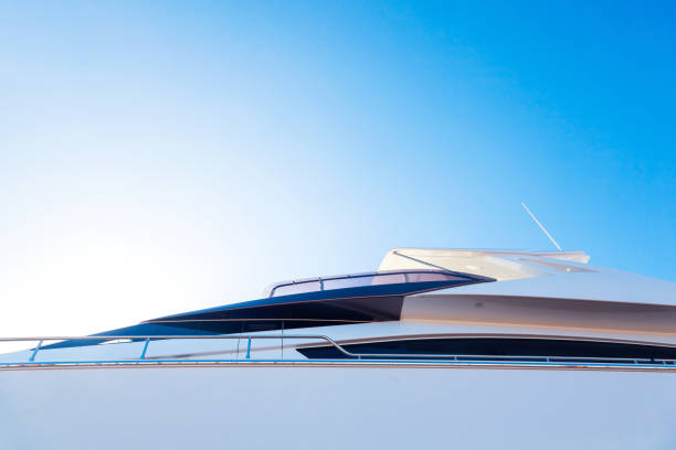 the hull of a luxury, motor, white yacht, with portholes on it, against the blue sky and the light of the sun in the corner, bottom view. - bow building imagens e fotografias de stock