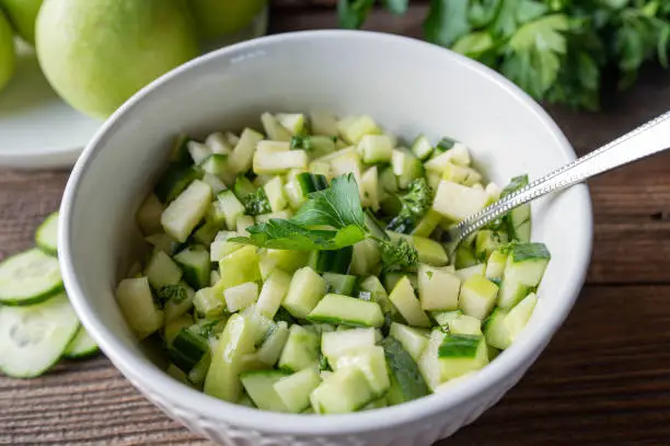 Delicious summer detox snack with marinated cucumber, green apple salad. Served ready to eat in a bowl with spoon on wooden table.