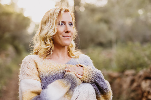 Smiling woman man with hands on chest and grateful face gesture standing in a forest. Useful for healthy, mindfulness, consciousness, awareness and self love concepts. Very selective focus and added grain. Part of a series.