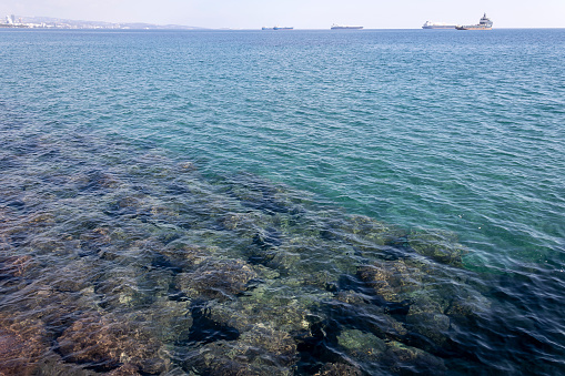 Aquamarine sea water with rocks underwater and ships on the horizon, Limassol, Cyprus