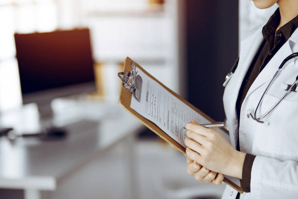 istock Unknown female doctor using clipboard in sunny clinic. Medicine concept 1483569871