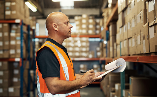 Clipboard, checklist and man in warehouse, logistics or factory for inspection of stock inventory, storage boxes or courier. Serious person or manager writing notes or documents in package management