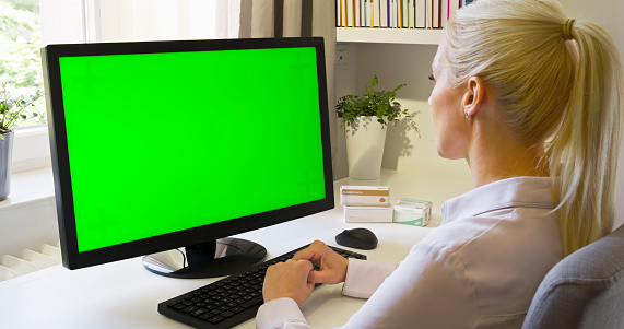 Side view of woman using green screen of computer monitor in home office.