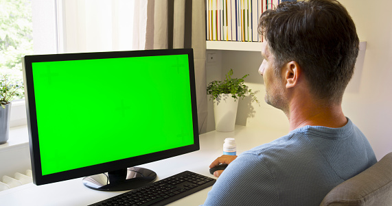 Man working at green screen of computer monitor in home office.