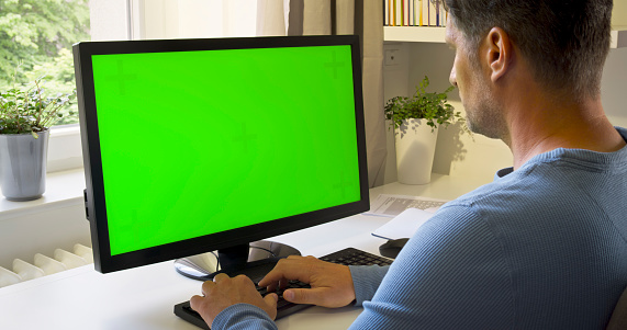 Mature man working at green screen of computer monitor in home office.