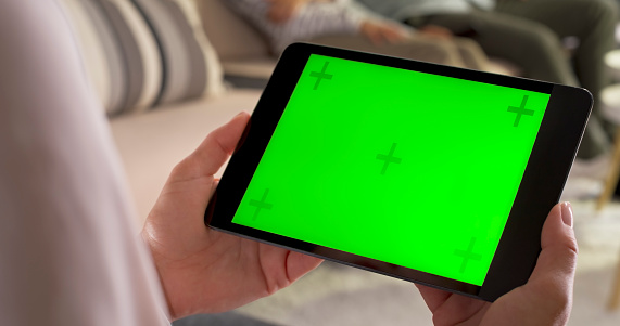 Close-up of woman's hands using green screen of digital tablet at home.