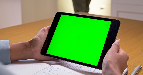 Close-up of woman's hands using green screen of digital tablet at home.