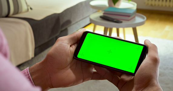 Close-up of man's hands using green screen of smart phone at home.
