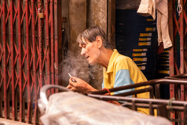 smoking tobacco in an old warehouse alley at Warorot Market Chiang Mai, Thailand  - March 20, 2023 : Unidentified elderly man smoking tobacco in an old warehouse alley at Warorot Market , Chiang Mai, Thailand. warorot stock pictures, royalty-free photos & images