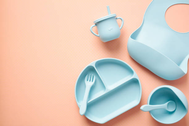 istock Baby feeding set on color background. Flat lay silicone bowls, divided plates, sippy, bib. Self feeding eating utensils top view. 1483587239