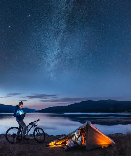 Couple on bike adventure trip with tent near lake at night.