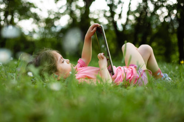 Little girl is playing on her tablet instead playing on the lawn in the yard