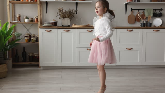 Cute barefooted little girl in ballet skirt dancing at home