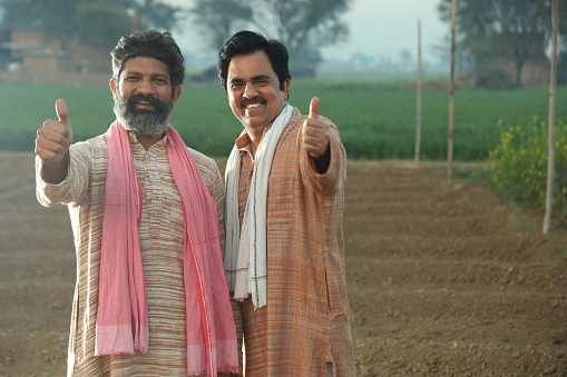 Happy Indian farmers standing in the mustard field and enjoying the benefits from the flourished rural mustard crop