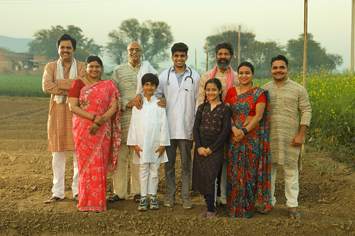 Large family together standing in a mustard field with a doctor looking towards the camera confidently and happily.