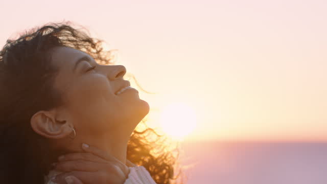 portrait of beautiful hispanic woman enjoying peaceful seaside at sunset exploring mindfulness contemplating spirituality with wind blowing hair