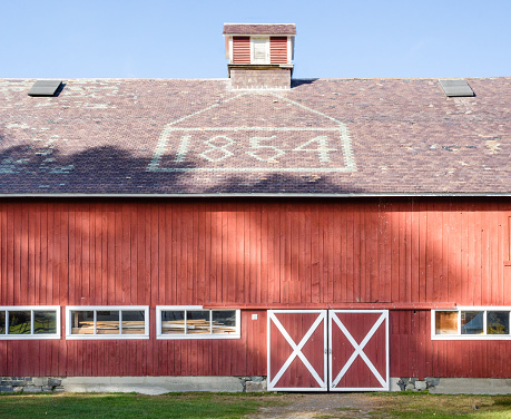 Red New England Barn with date 1854 spelled out in stone on slate roof. Shadows on sunlit barn, clear blue sky