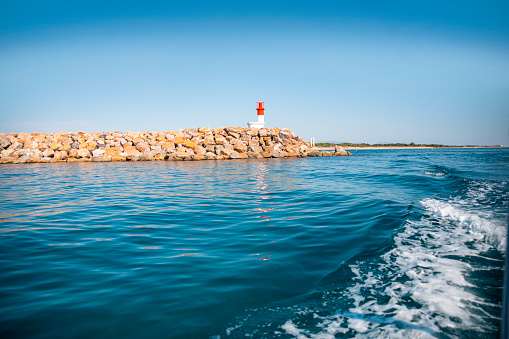 Red and White Lighthouse at stone island in the blue sea. Solitary navigation lighthouse at rocky pier. Copy space