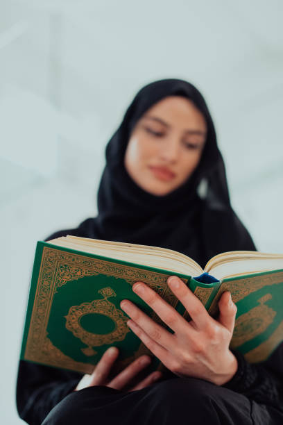 istock Young traditional muslim woman reading Quran on the sofa before iftar dinner during a ramadan feast at home 1483612269