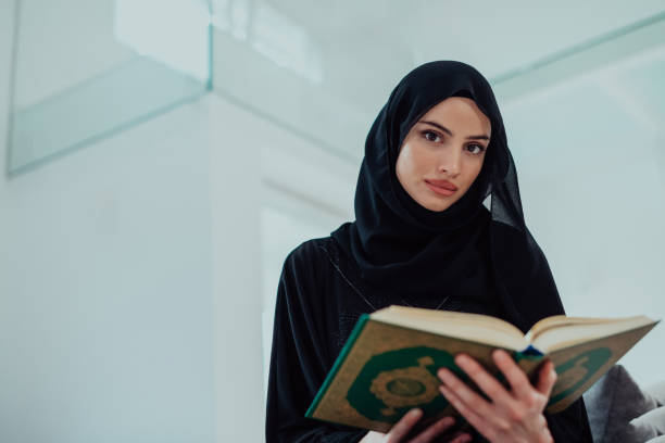 istock Young traditional muslim woman reading Quran on the sofa before iftar dinner during a ramadan feast at home 1483612298