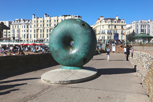 Brighton, United Kingdom - April 15, 2022: 'A public artwork by Hamish Black on Brighton seafront, UK. The sculpture is a circular donut shaped globe cast in bronze. Bronze sculpture on a groyne next to Brighton Palace Pier, Sussex, GB.